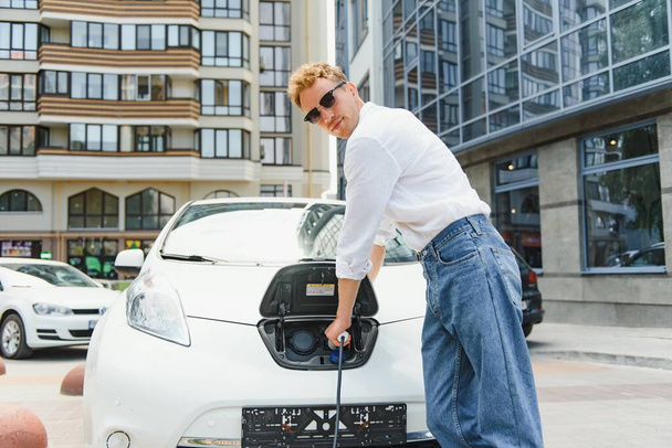 A handsome young man is charging his modern electric car. - Valokuva, kuva