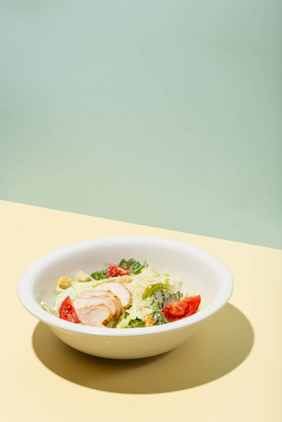 Caesar salad in white plate on yellow hard shadow modern - Foto, afbeelding