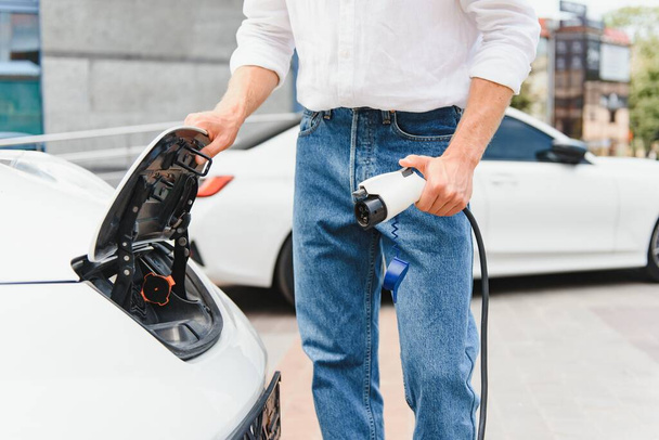 Stylish man inserts plug of the charger into the socket of electric car close-up - Foto, Imagen