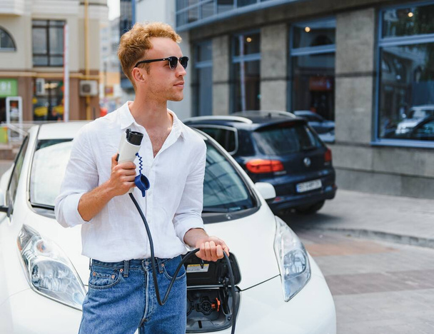 A handsome young man is charging his modern electric car. - Fotoğraf, Görsel