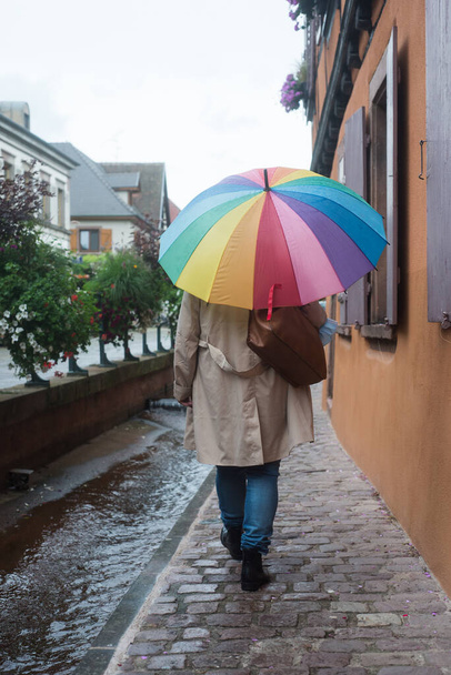 Portrait on back view of woman with a rainbow umbrella walking in the street - Zdjęcie, obraz