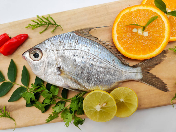 Gerres Fish (Gerres Filamentosus), Whipfin srebrna biddy Fish, ozdobiona liśćmi curry i pomidorem na drewnianej podkładce, białe tło.. - Zdjęcie, obraz