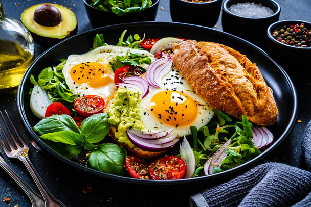 Sunny side up eggs on bun with fresh green vegetables, mini tomatoes and guacamole on wooden table  - Fotoğraf, Görsel