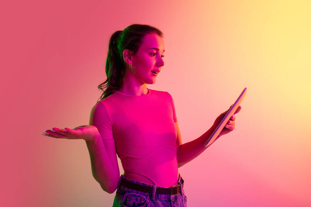 Immagine ritagliata di giovane ragazza che legge notizie da tablet isolato su sfondo studio gradiente in luci al neon - Foto, immagini