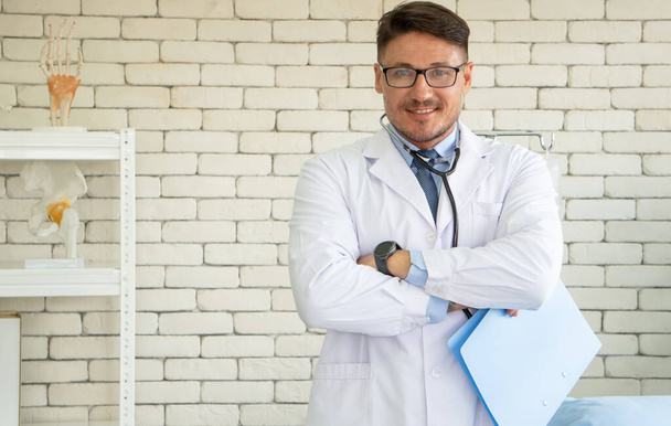 Retrato homem branco médico de pé com os braços cruzados sorriso confiante amigável na mesa na clínica. Cirurgião Ortopedista Consulta Médica no Hospital - Conceito. - Foto, Imagem