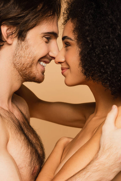 side view of shirtless man and topless woman smiling at each other face to face isolated on beige - Foto, afbeelding