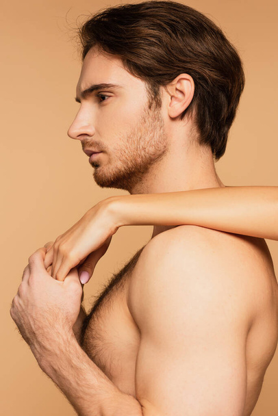 vista lateral del hombre sin camisa cogido de la mano de una mujer joven aislada en beige - Foto, imagen