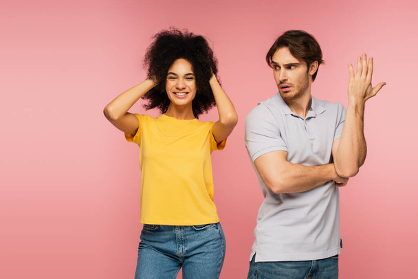 displeased man gesturing near cheerful latin woman touching head isolated on pink - Foto, Imagem