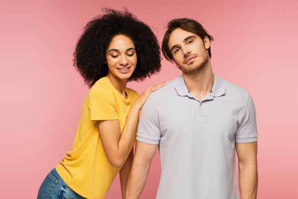 curly hispanic woman leaning on shoulder of young man looking at camera isolated on pink - Foto, Bild