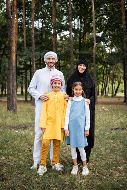 Arabian parents hugging smiling children in park  - Фото, изображение