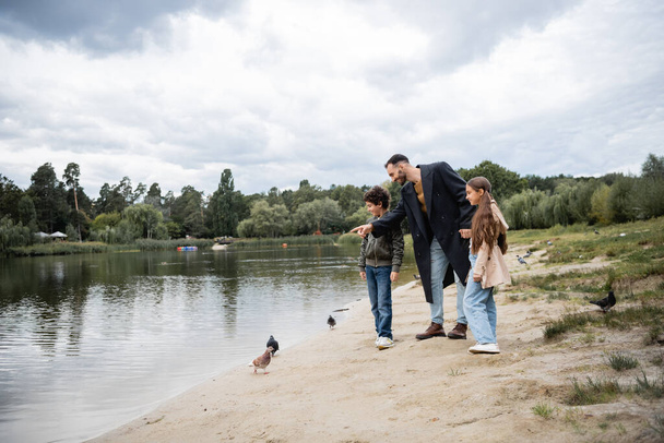 Crianças árabes de pé perto do pai apontando para o lago no parque  - Foto, Imagem