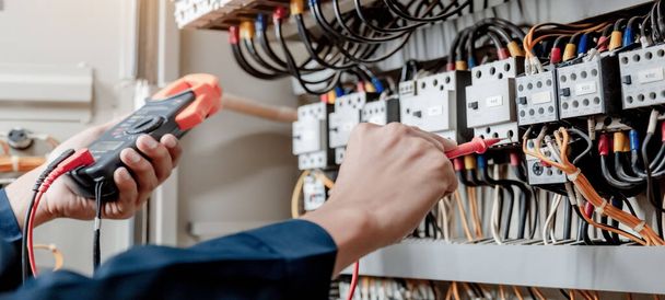 Electrician engineer uses a multimeter to test the electrical installation and power line current in an electrical system control cabinet. - Photo, Image