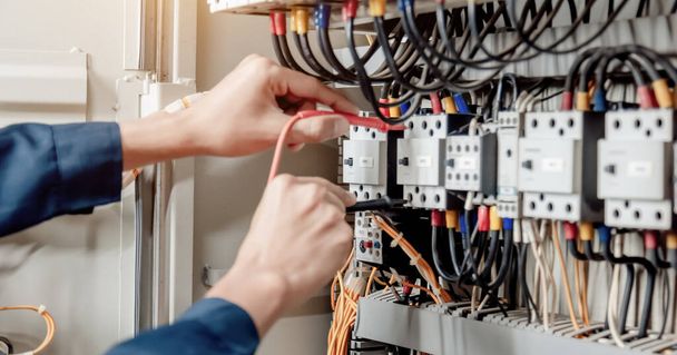 Engenheiro eletricista usa um multímetro para testar a instalação elétrica e corrente de linha de energia em um gabinete de controle do sistema elétrico. - Foto, Imagem