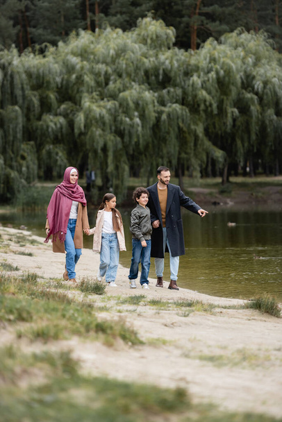 Hombre musulmán señalando el lago cerca de los niños y la esposa en el parque  - Foto, imagen
