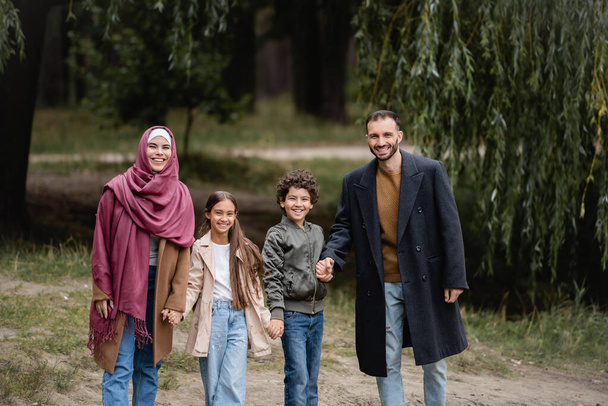 Cheerful muslim parents walking near kids in park in autumn  - Fotoğraf, Görsel