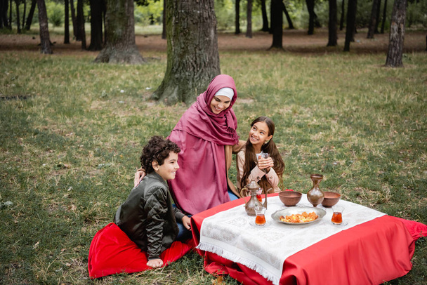 Muslim mother sitting near kids during picnic in park  - Zdjęcie, obraz