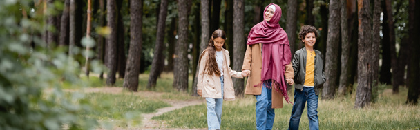 Arabian woman in traditional hijab walking near kids in autumn park, banner  - Photo, Image