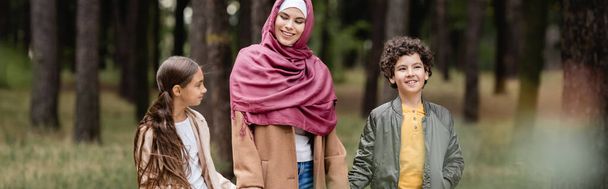 Iloinen muslimipoika kävelee lähellä äitiä ja siskoa puistossa, banneri  - Valokuva, kuva