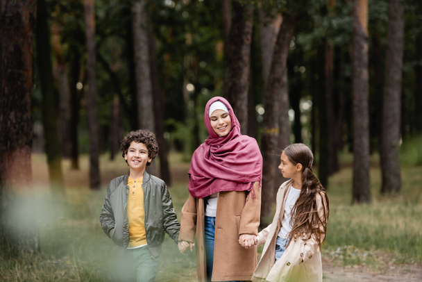 Muslim woman in hijab holding hands of children in park  - Photo, Image