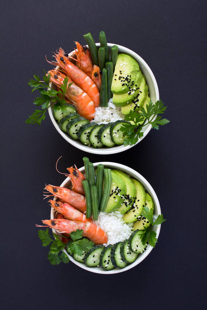 Vue du dessus de la salade de poke avec crevettes rouges et légumes verts dans les bols blancs sur le fond noir. Emplacement vertical. - Photo, image