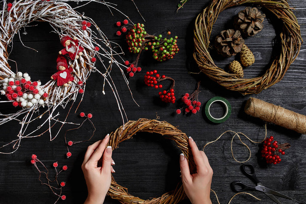 Top view of female hands make a Christmas wreath. Packed gifts and scrolls, spruce branches and tools on wooden table. - Valokuva, kuva
