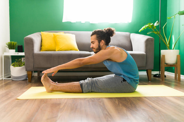 Voorwaarts buigen yoga pose. Fit hispanic man stretching zijn armen en benen tijdens het sporten thuis  - Foto, afbeelding