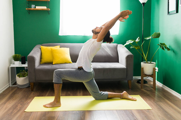Relaxed young man in a crescent lunge pose on a yoga mat. Stretching his body with a morning workout - Foto, Imagem