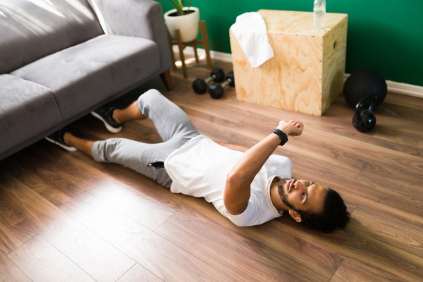Používám svého chytráka během cvičení. Sportovní latin muž ležící na podlaze při cvičení a při pohledu na zdravotní aplikaci - Fotografie, Obrázek