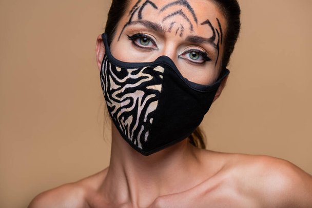 young model with tiger makeup and animal print mask looking away isolated on beige - Valokuva, kuva