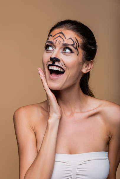 mujer excitada con hombros desnudos y maquillaje de tigre posando aislado en beige - Foto, Imagen