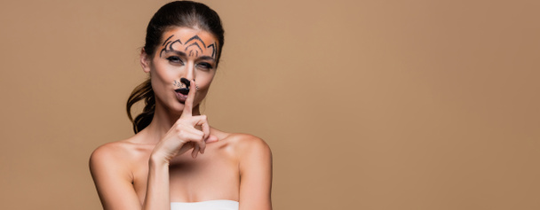 mladá žena s holými rameny a tygřím make-upem ukazující na béžové, prapor - Fotografie, Obrázek