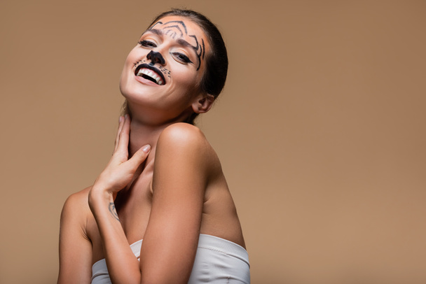 young and positive woman with bare shoulders and tiger makeup posing isolated on beige - Valokuva, kuva