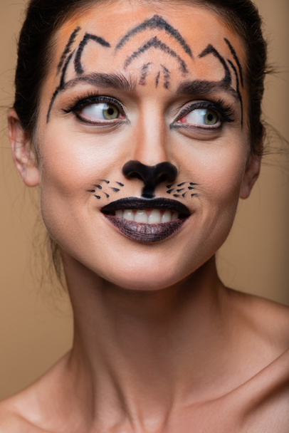 close up of joyful woman with tiger makeup looking away isolated on beige - 写真・画像