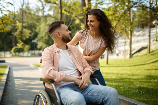 Молодая пара с инвалидной коляской прогуливается по парку - Фото, изображение