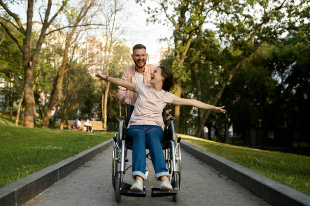 Χαρούμενο ζευγάρι αγάπης με αναπηρική καρέκλα βόλτες στο πάρκο - Φωτογραφία, εικόνα