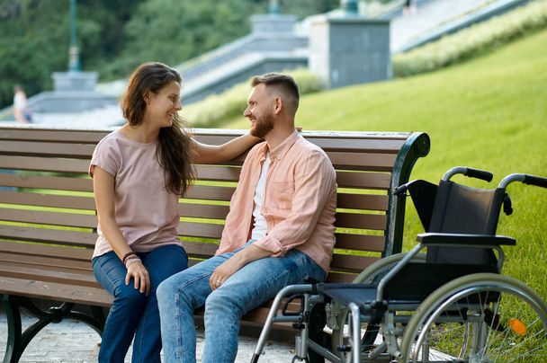 Couple with wheelchair relaxing on bench in park - Foto, Imagen