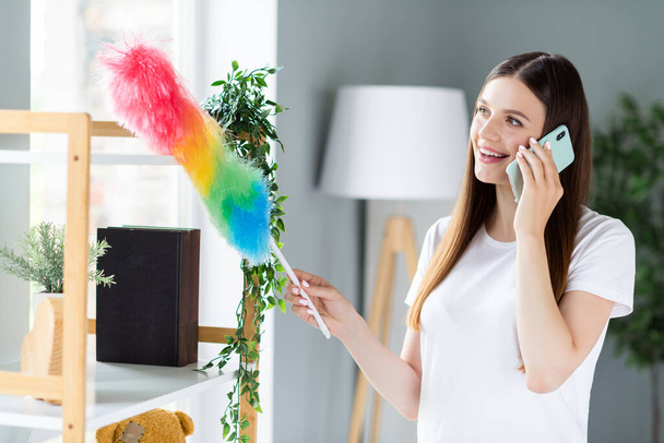 Portrait of attractive cheerful girl cleansing dust fluffy tassel talking on phone order service at home living room indoors - Photo, Image