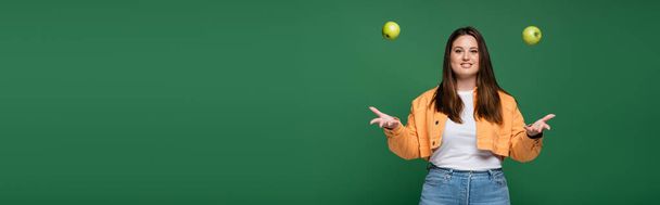 Femme gaie avec excès de poids jetant des pommes isolées sur vert, bannière  - Photo, image