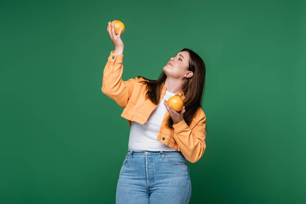Young body positive woman holding fresh oranges isolated on green  - 写真・画像