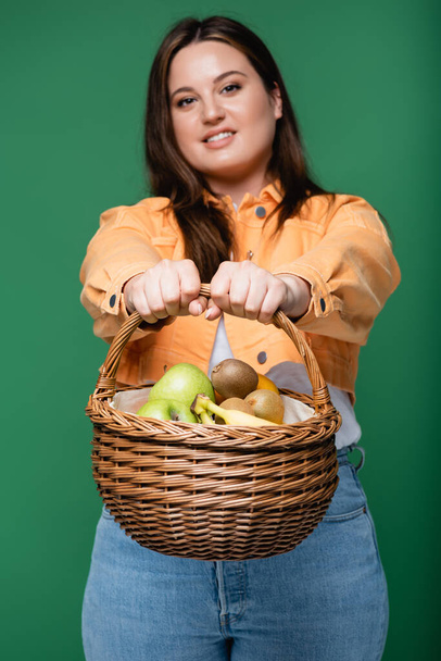 Cesta con frutas en manos de mujer borrosa con sobrepeso aislado en verde  - Foto, imagen