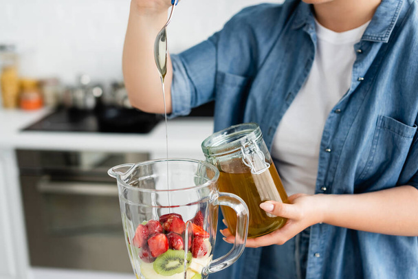Cropped view of plus size woman pouring honey in blender with fruits - Photo, Image