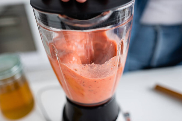 Cropped view of smoothie in blender near blurred woman in kitchen  - Valokuva, kuva