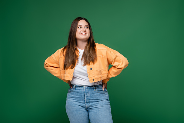 Cheerful plus size woman holding hands on hips isolated on green  - Foto, Imagem