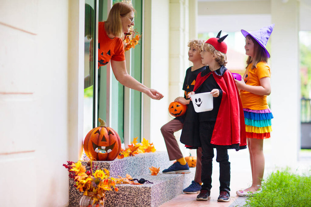 Kids trick or treat on Halloween night. Child at decorated house door. Boy and girl in witch and vampire costume and hat with candy bucket and pumpkin lantern. Woman with sweets.  - Photo, Image