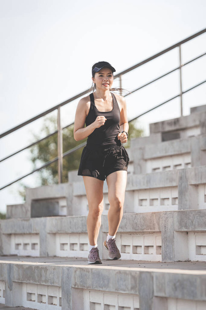 A healthy adult Asian woman running up on concrete stairs of the city stadium to strengthen body - Fotografie, Obrázek
