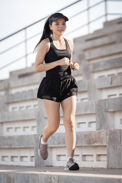 Zdrowa, dorosła Azjatka biegnie po betonowych schodach stadionu, aby wzmocnić ciało - Zdjęcie, obraz