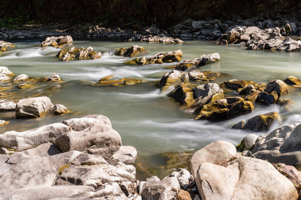 Гладкая вода и камни, река и дикая природа, горы, маленький водопад - Фото, изображение