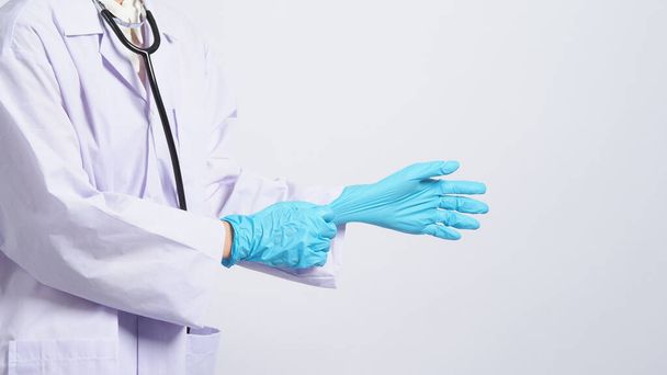 Käsineet kädessä. Aasialainen lääkäri käyttää sinistä kuminitriilikäsinettä. Tohtori naamioituneena hanskat käteen. erillinen valkoinen taustakopiotila. Terveydenhuollon suojaaminen - koronoviruspandemia. - Valokuva, kuva