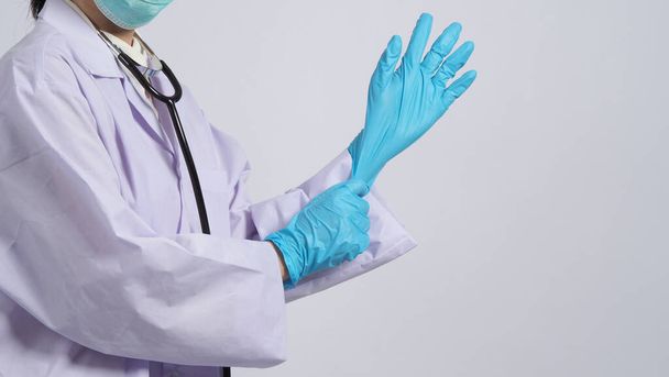 W rękawiczkach. Lekarz azjatycki nosi niebieską gumową rękawicę nitrylową. Doktor w masce założył rękawiczki. odizolowane białe tło miejsca kopiowania. Koncepcja pandemii koronowirusa w ochronie zdrowia. - Zdjęcie, obraz