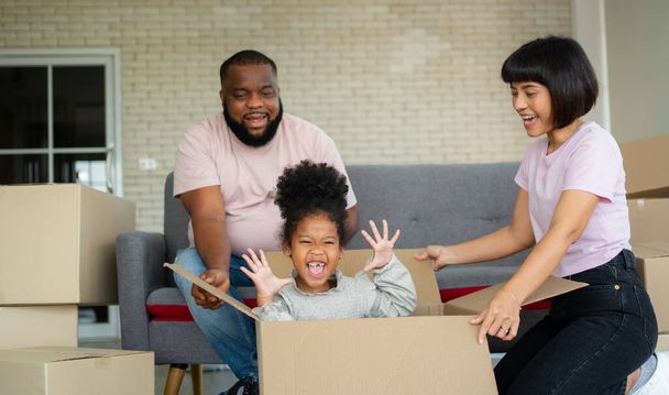Karışık Irk aileleri, emlak satın aldıktan sonraki ilk gün yeni bir eve taşındıktan sonra dinlenmek için kanepede oturuyorlar. Yeni bir aile için yeni bir hayata başlama kavramı. - Fotoğraf, Görsel